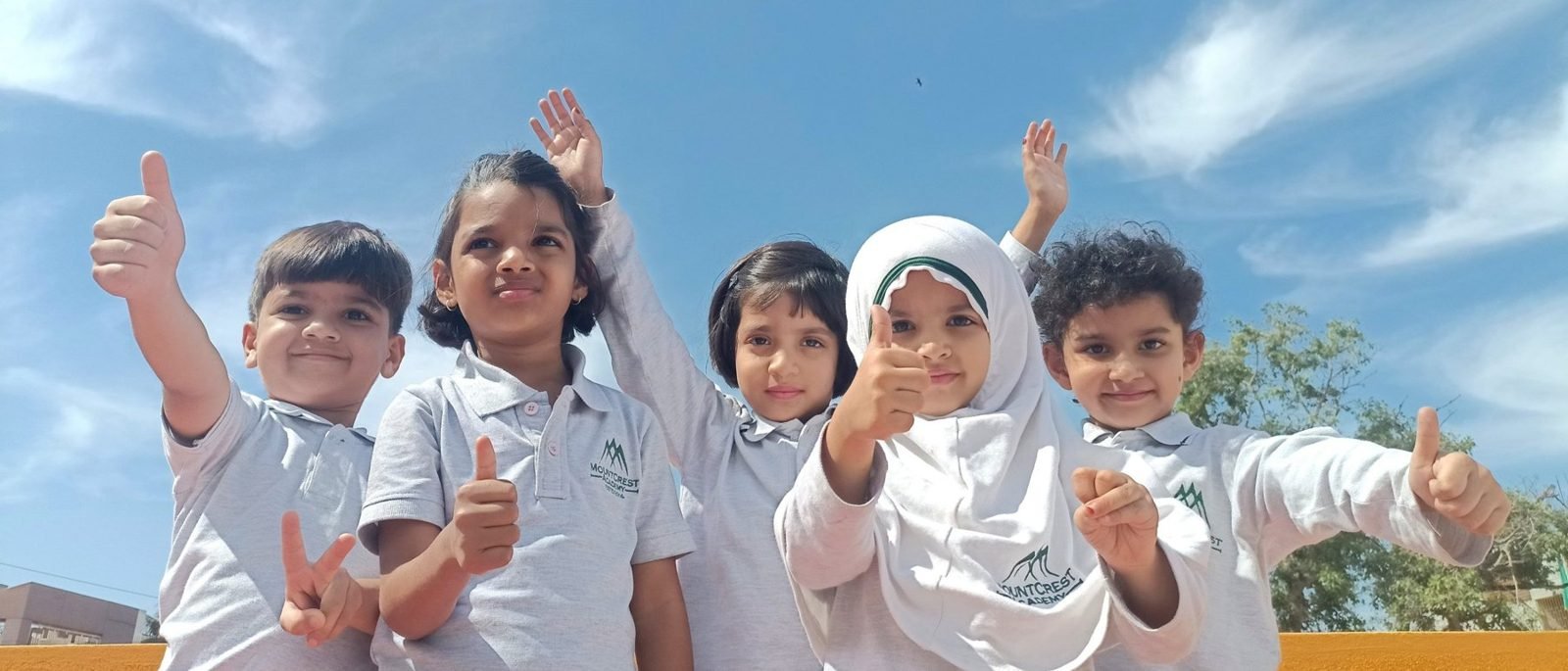 Smiling Mountcrest Prep students give a thumbs up under a blue sky